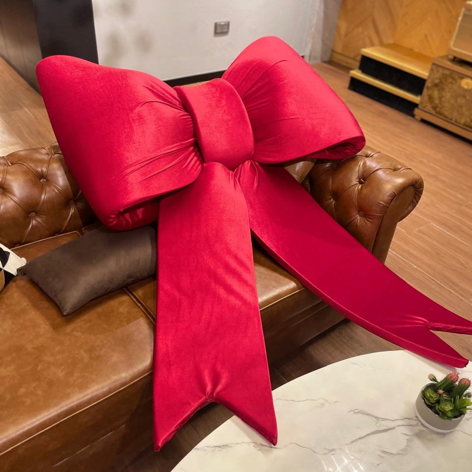 Large red bow-shaped pillow on a brown leather sofa in a living room.