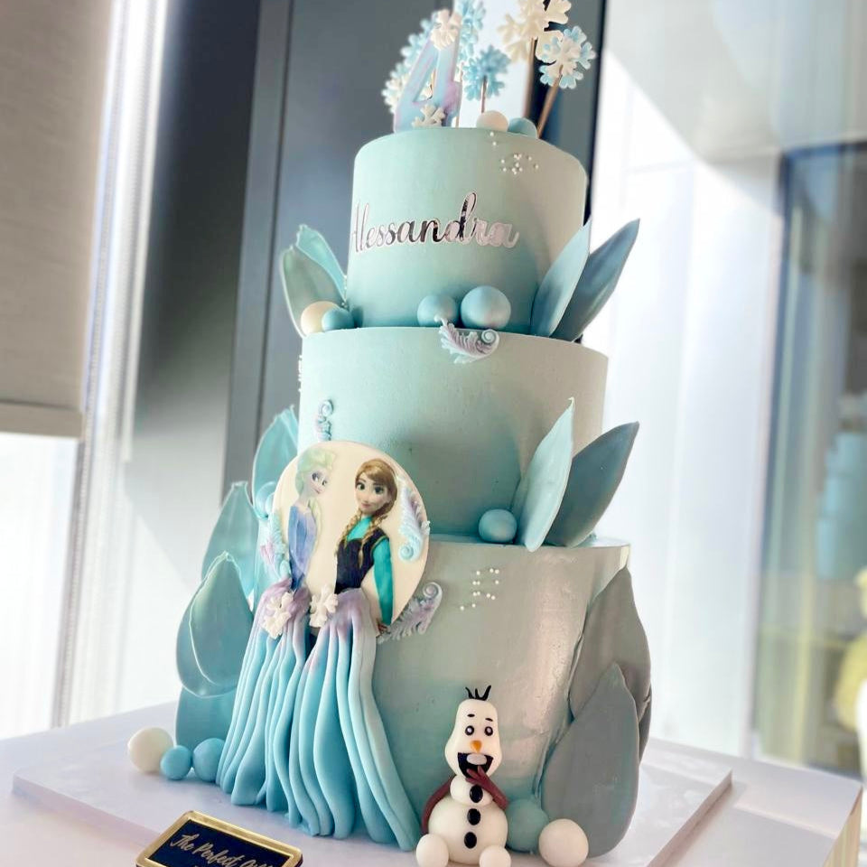 Three-tiered cake with Frozen theme decorations on a white surface.