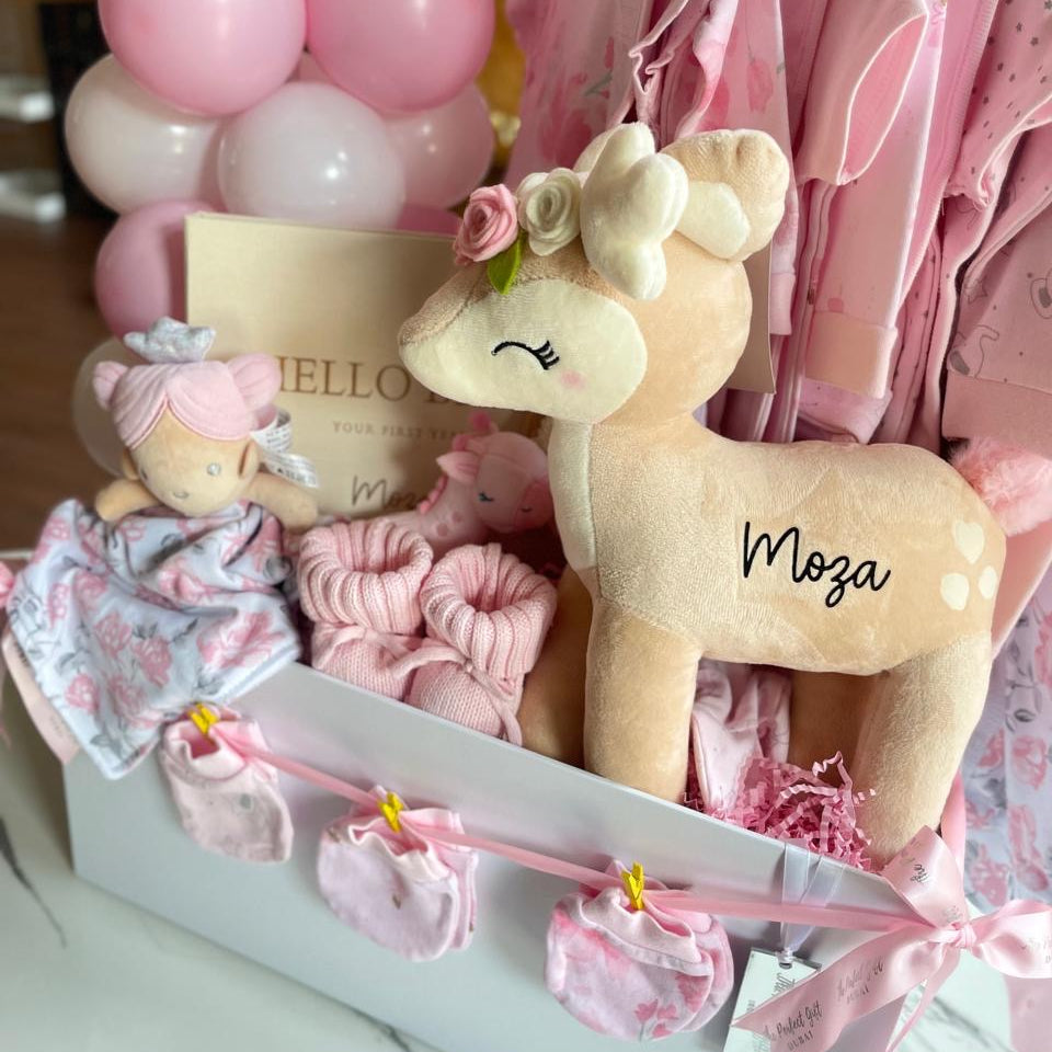 Baby girl gift set with plush toy, clothes, and balloons in a box.
