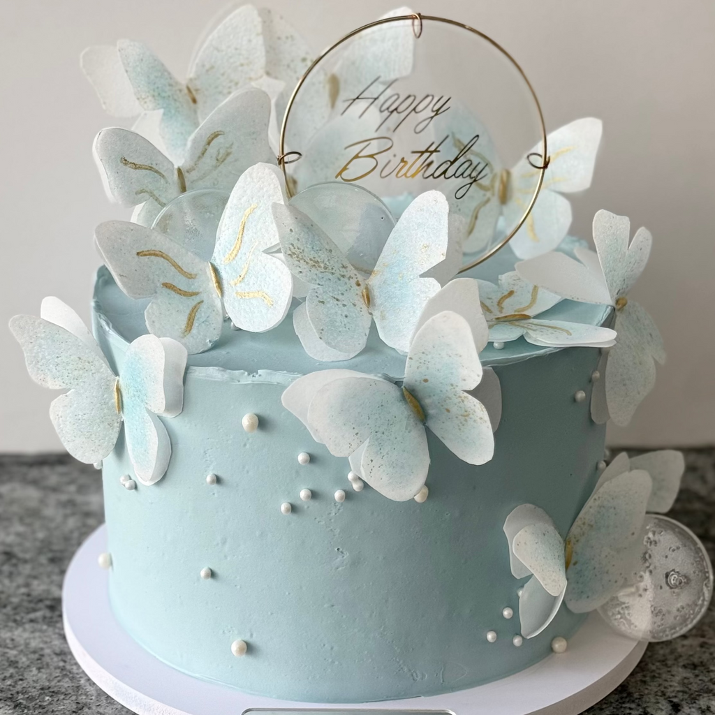 Light blue birthday cake with butterfly decorations and 'Happy Birthday' text on a neutral background.
