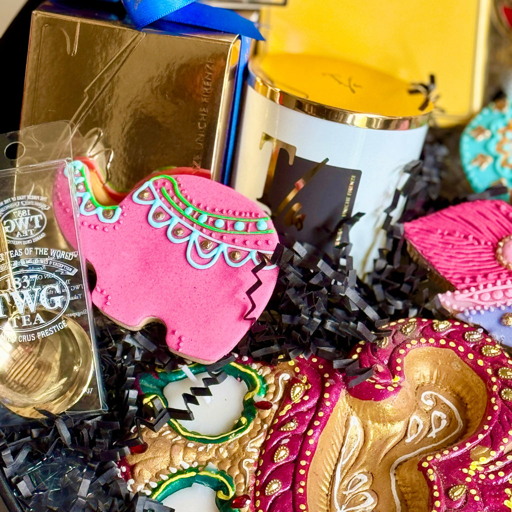 Decorative items including a pink and gold mask, a gold box, and a white candle with a blue ribbon on a black background.