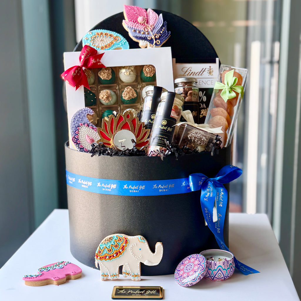 Gift basket with various items including a Lindt chocolate bar, cookies, and a small elephant figurine on a white surface.