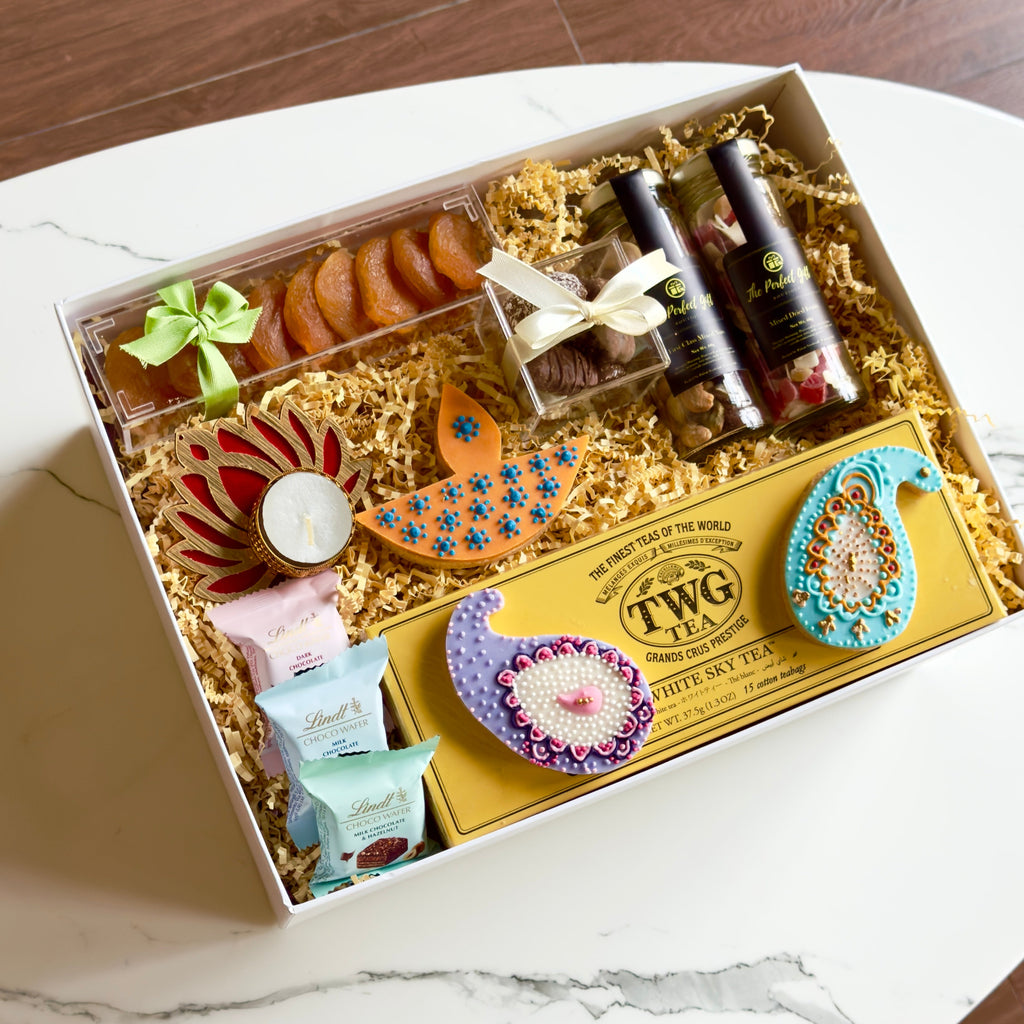 Gift box with assorted items including cookies and tea packaging on a marble surface.
