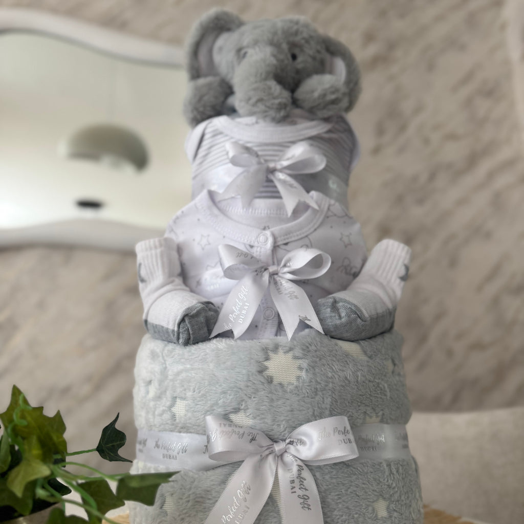Three-tiered baby diaper cake with elephant toy on top, featuring gray and white colors.