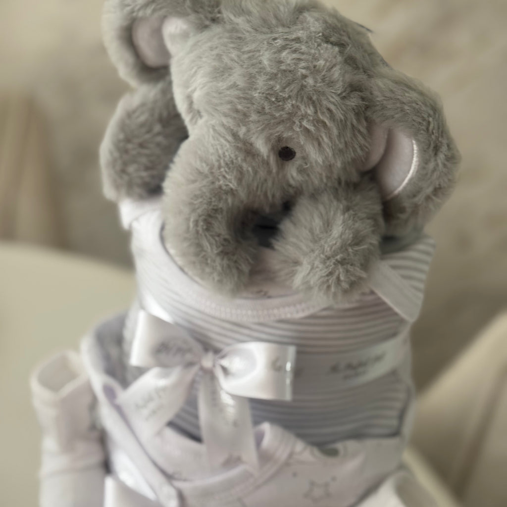Gray plush elephant toy wrapped in white cloth with a bow, on a beige background