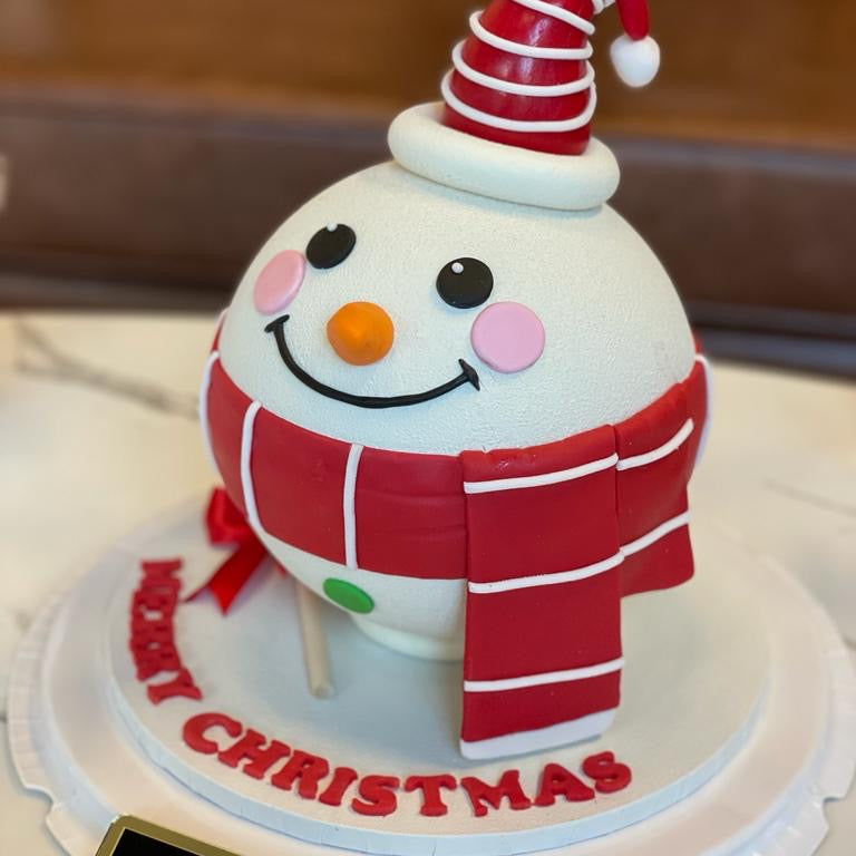 Christmas-themed cake with a snowman design, red scarf, and Santa hat on a white plate.