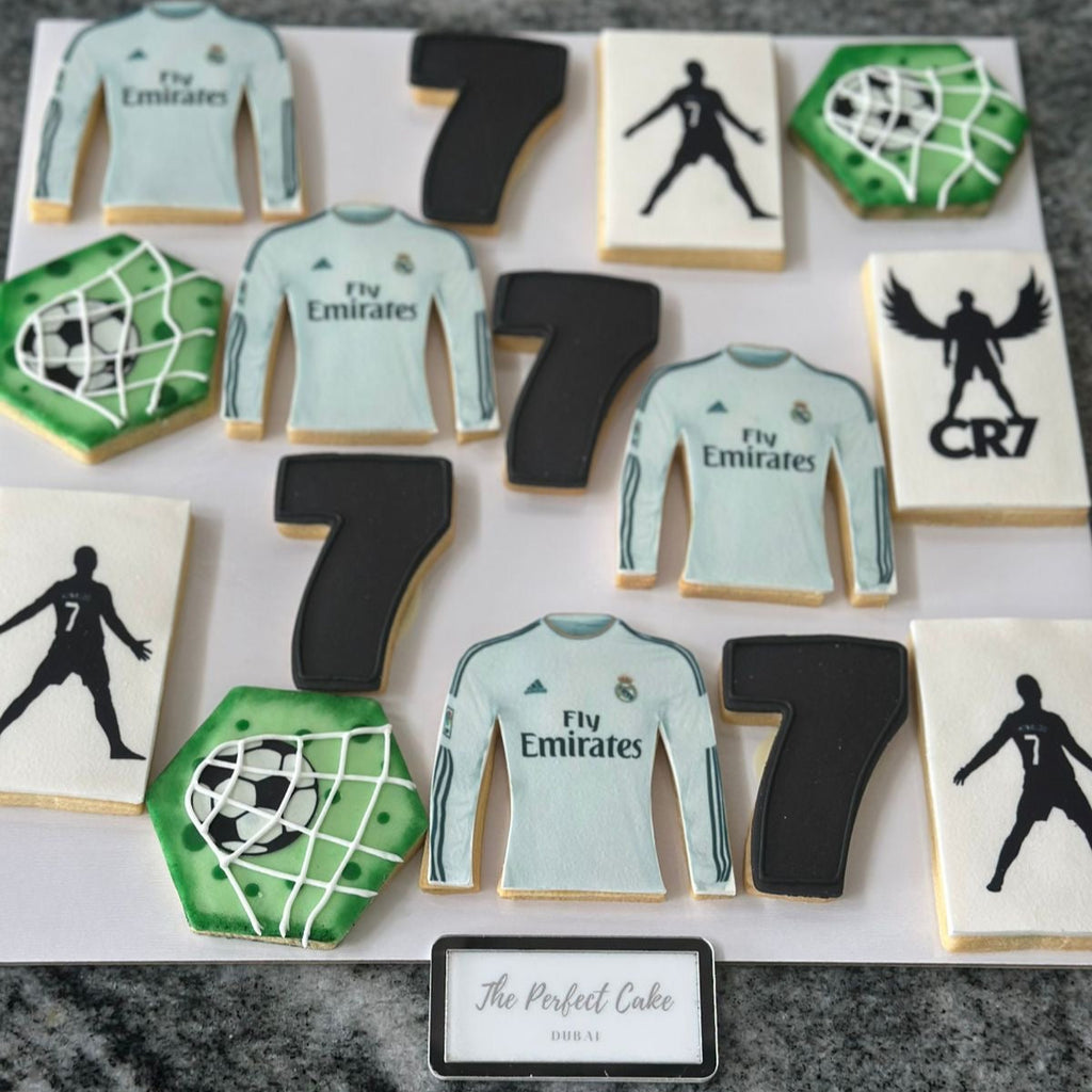 Cookies designed to resemble soccer jerseys, numbers, and a goal net on a white tray.