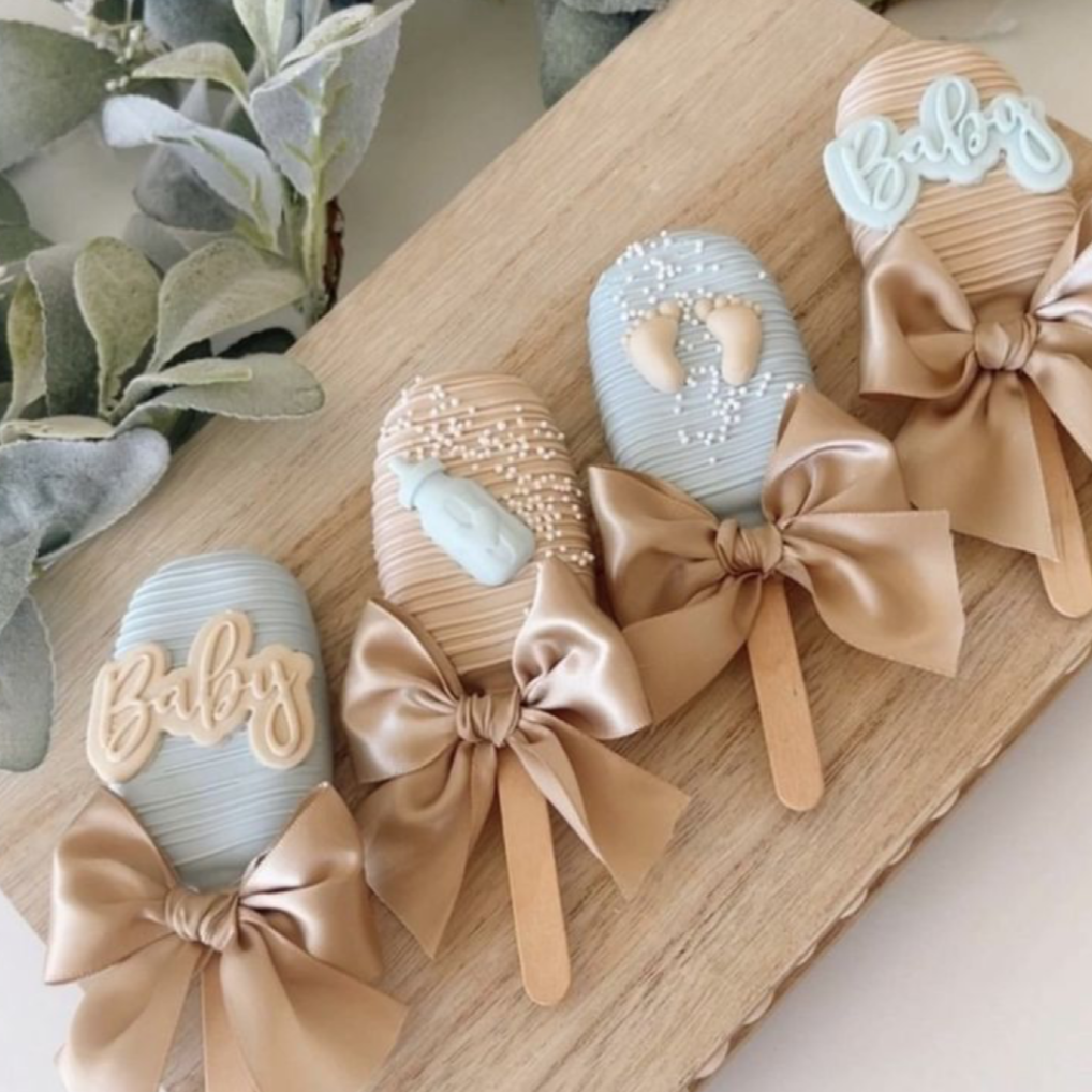 cakesicles with bows and 'Baby' text on a wooden surface