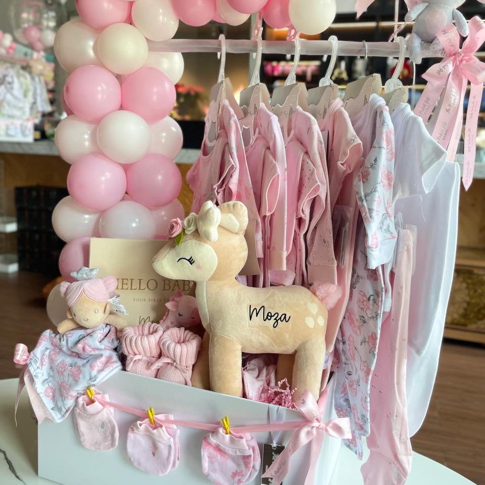 Baby shower setup with pink and white balloons, baby clothes, and plush toys.