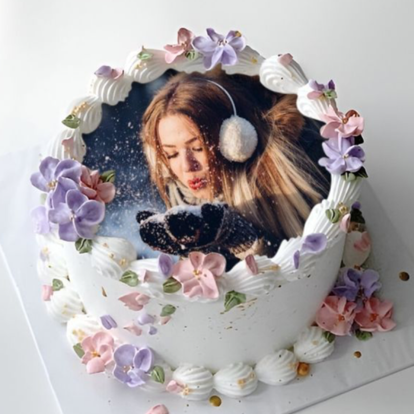Decorative cake with a photo of a person and a cat on top, surrounded by flowers.