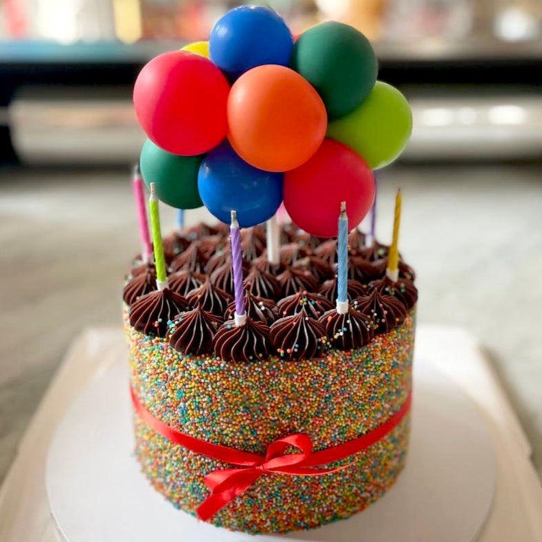 Colorful birthday cake with balloons and candles on a white plate.