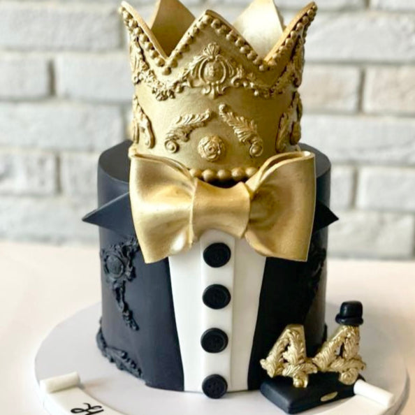 Cake with gold crown and bow tie against a white brick wall