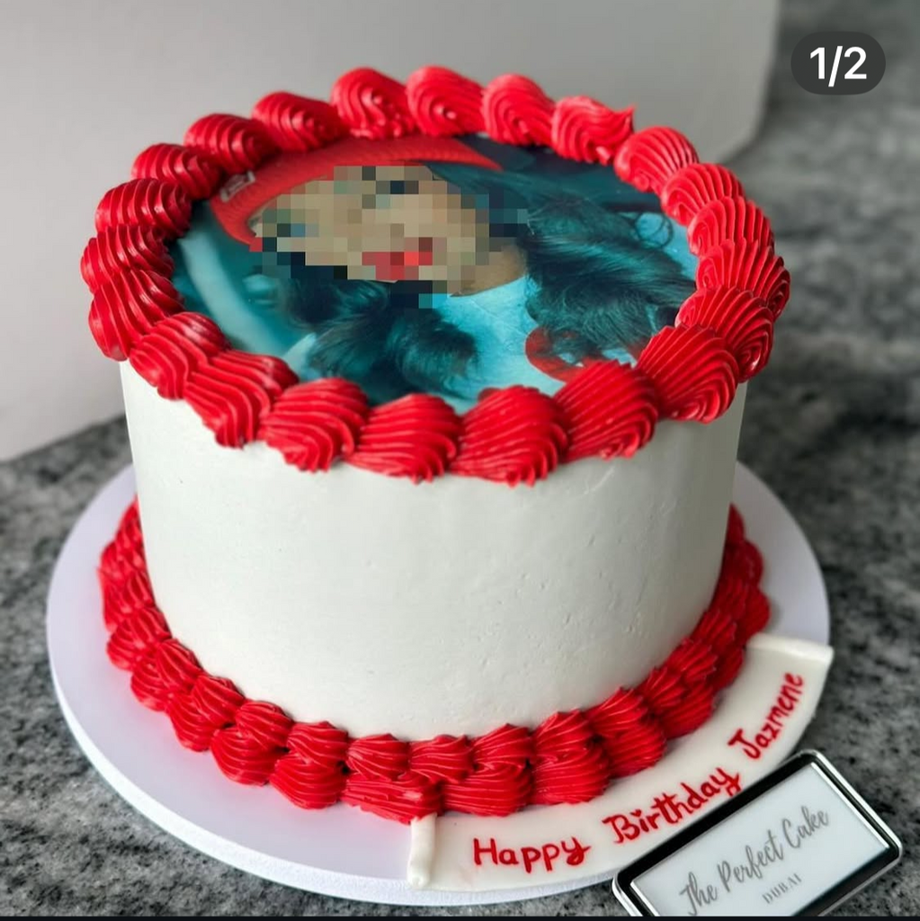 Birthday cake with red decorations and a photo of a child on top, displayed.
