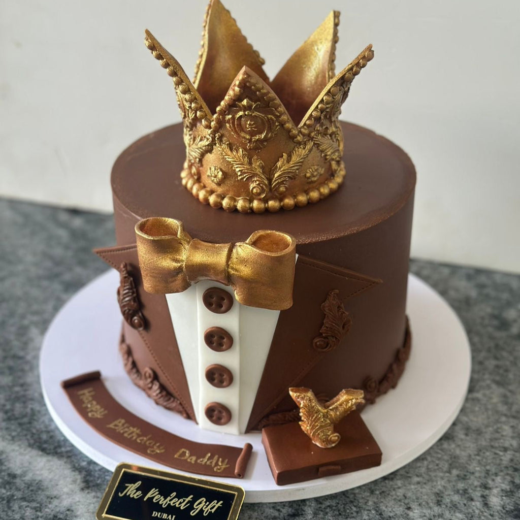 Chocolate cake with gold crown and bow tie on a white plate