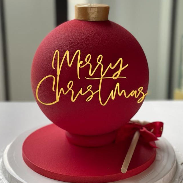 Red Christmas ornament with 'Merry Christmas' text on a stand, featuring a gold top and black label.