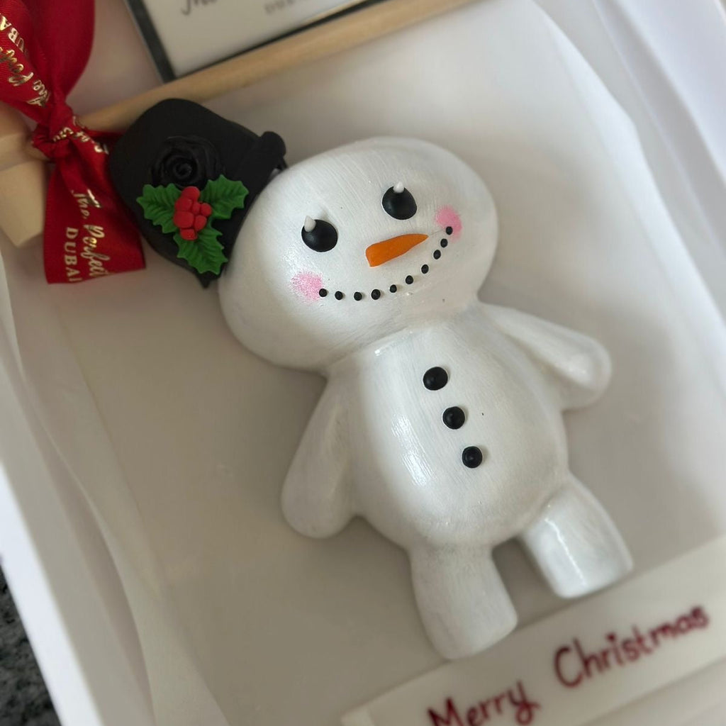 Snowman figurine with festive decorations in a box labeled 'Merry Christmas'.