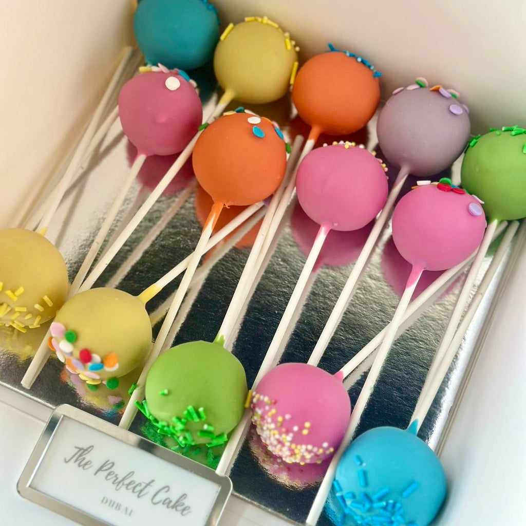 Colorful cake pops on sticks in a box with 'The Perfect Cake' label.