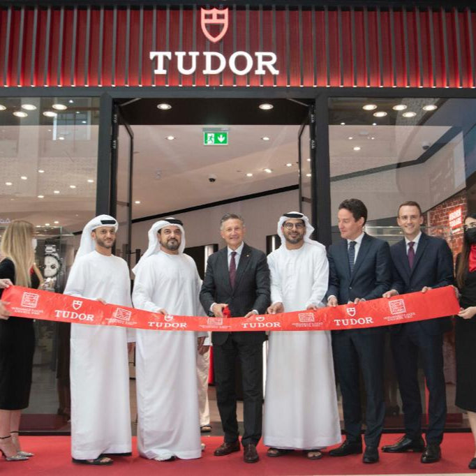Group of people cutting a ribbon in front of a Tudor store.