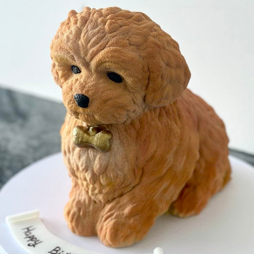 Dog-shaped cake with a bow tie on a white plate, featuring a personalized message.