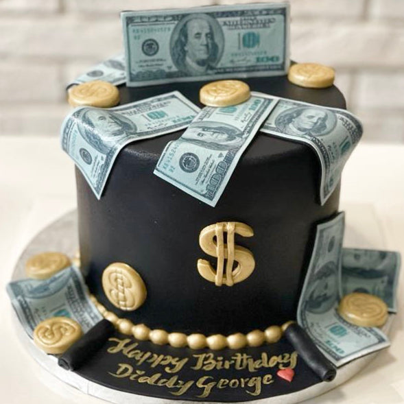 Black birthday cake with dollar bill decorations and a gold dollar sign on a white surface.
