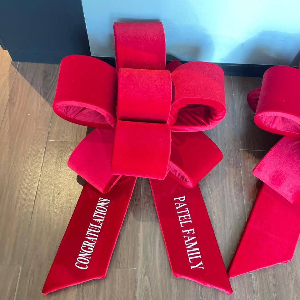 Red velvet bow with 'Congratulations Patel Family' text on a wooden floor.