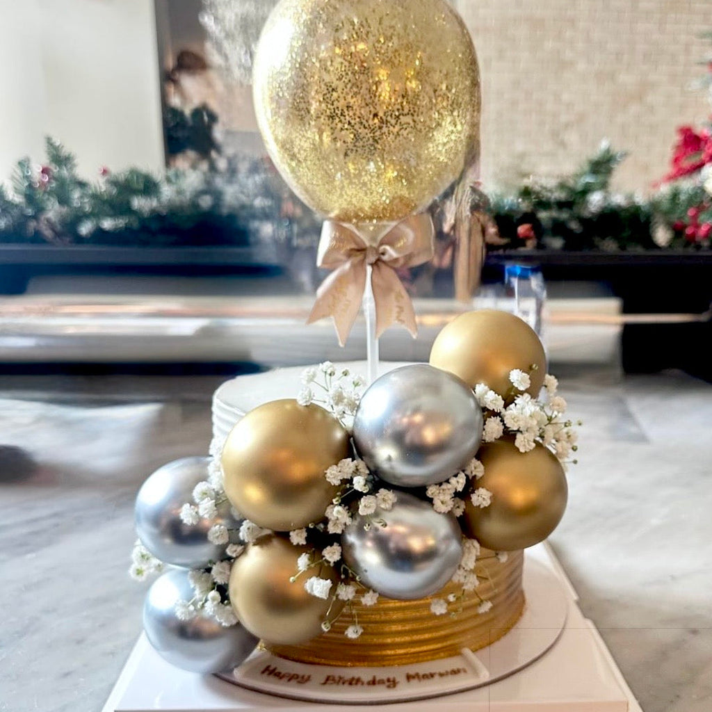 Decorative cake with gold and silver balloons in a room with Christmas decorations.