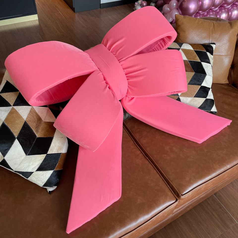 Large pink bow on a brown leather couch with decorative pillows.