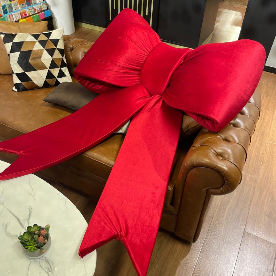 Large red bow on a brown leather couch in a living room setting.