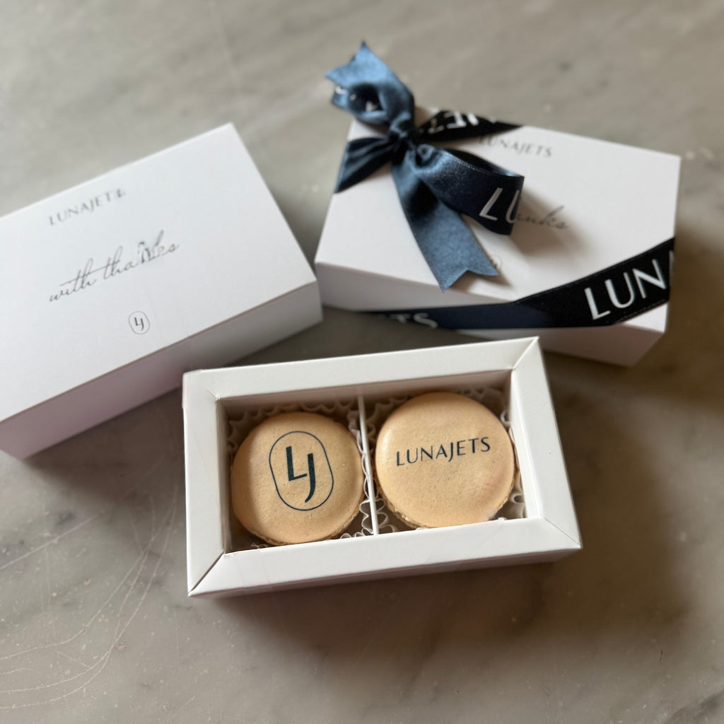 Two macaron items with 'Lunajets' branding in a white box on a marble surface.