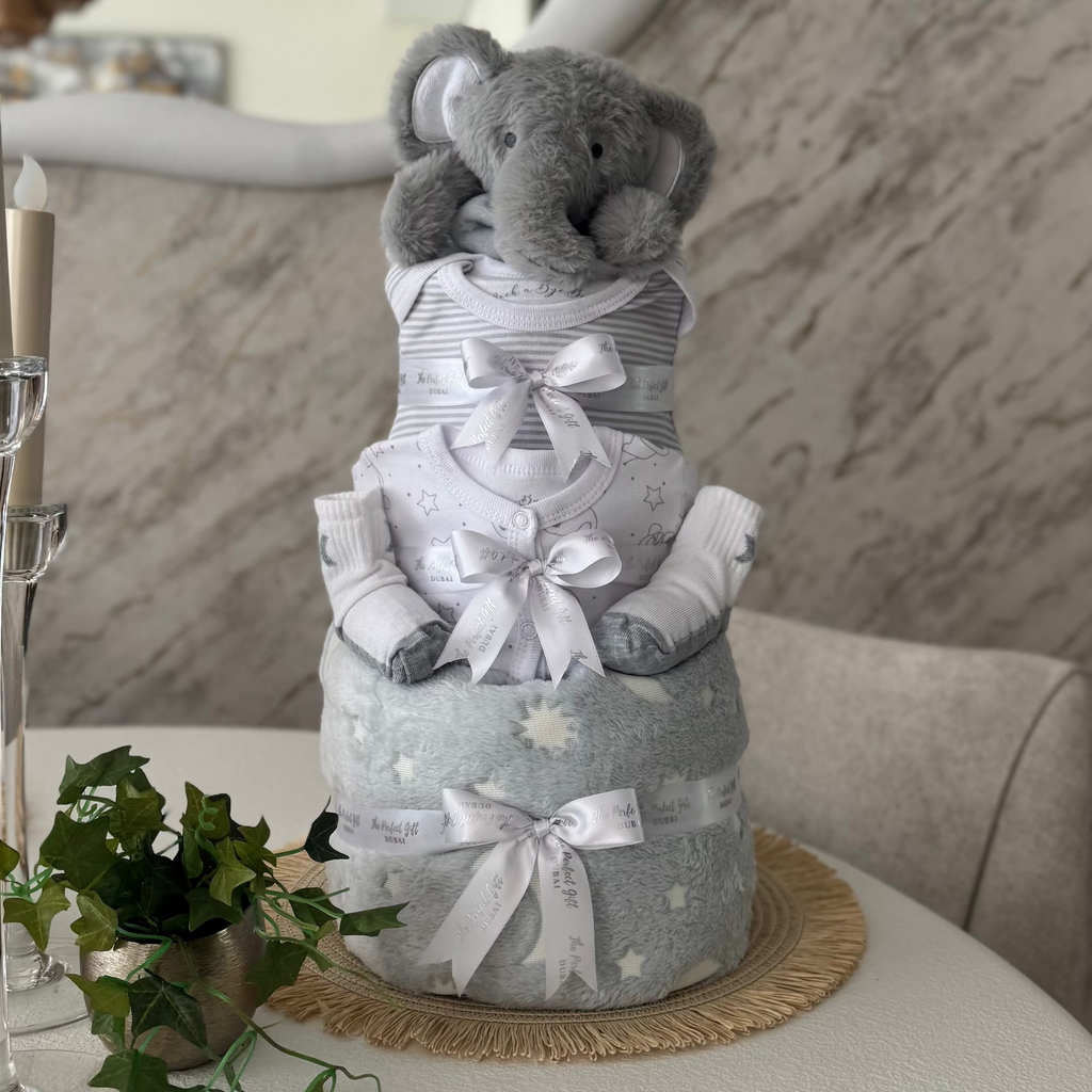 Three-tiered diaper cake with a plush elephant toy on a table with decorative elements.