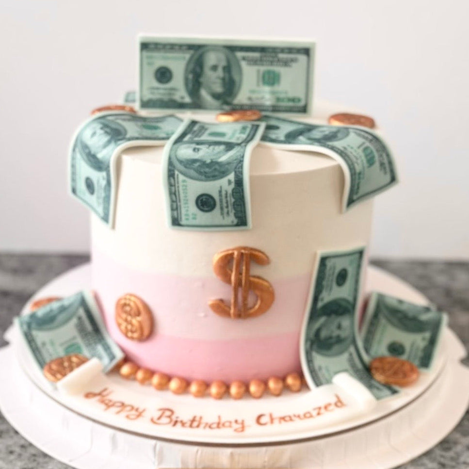 Two-tiered cake with dollar bill decorations and 'Happy Birthday' message on a marble surface.