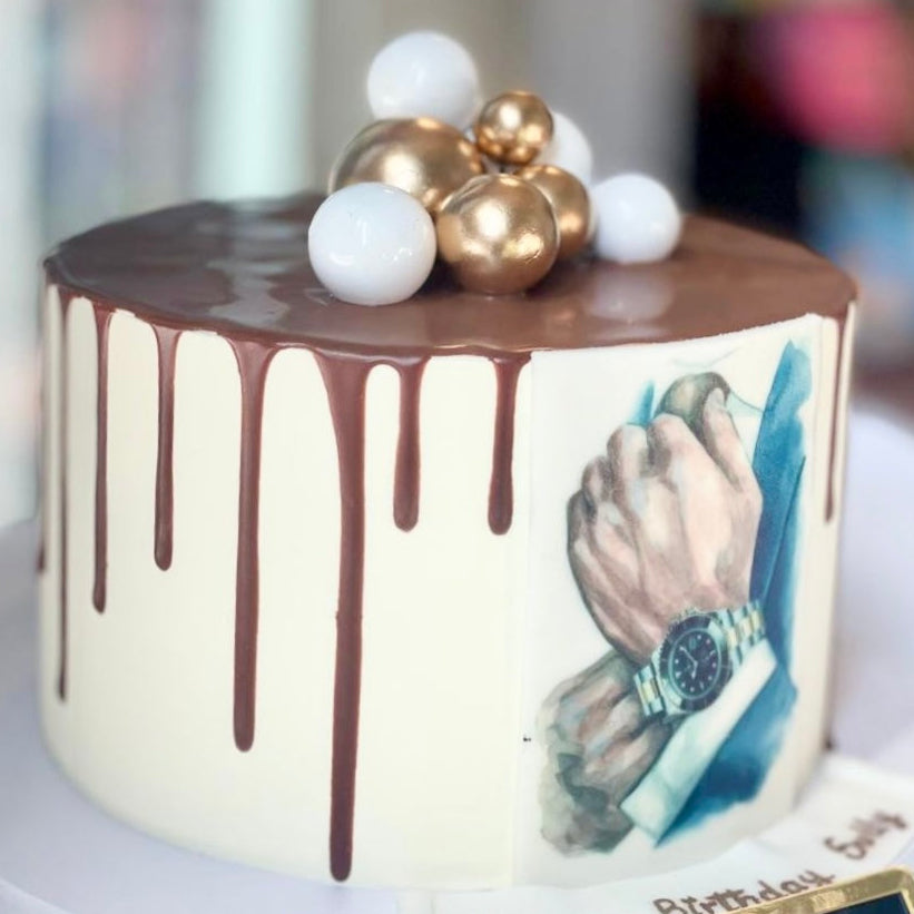 Cake with chocolate drizzle and a hand holding a watch design, topped with gold and white balloons.